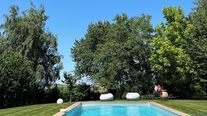 Une piscine sous un ciel bleu azur, entourée d’arbres verdoyants et d’une pelouse bien entretenue.
