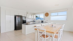 A modern kitchen with white cabinetry, a central island, and a dining area with white chairs and a wooden table. - Sanctuary Lodge by Ready Set Stay (Cowes)