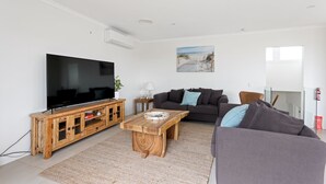A living room with a flat-screen TV, wooden entertainment unit, two sofas, a coffee table, and a beach-themed wall art. - Sanctuary Lodge by Ready Set Stay (Cowes)