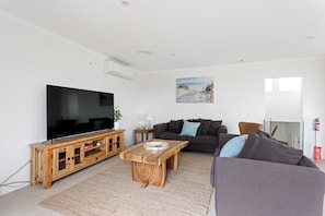 Ein Wohnzimmer mit Flachbildfernseher, Holzunterhaltungseinheit, zwei Sofas, einem Couchtisch und einem Wandbild mit Strandmotiv.