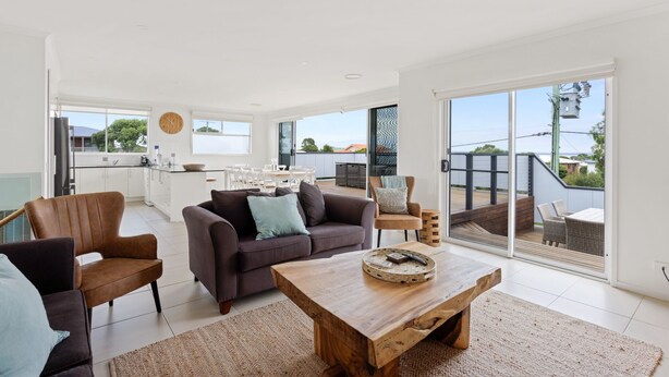 A modern living room with a sofa, chairs, and a coffee table. There is a kitchen area with white cabinets and a dining table. The room has large windows and a view of the outdoors. - Sanctuary Lodge by Ready Set Stay (Cowes)