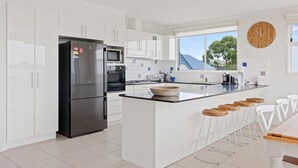 A modern kitchen with white cabinetry, a stainless steel refrigerator, a microwave, and a large island with bar stools. - Sanctuary Lodge by Ready Set Stay (Cowes)