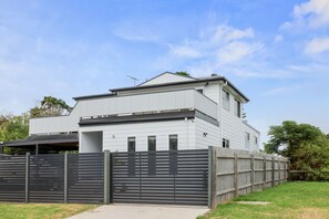 Ein modernes, zweistöckiges Haus mit flachem Dach, einer überdachten Veranda und einem eingezäunten Garten.