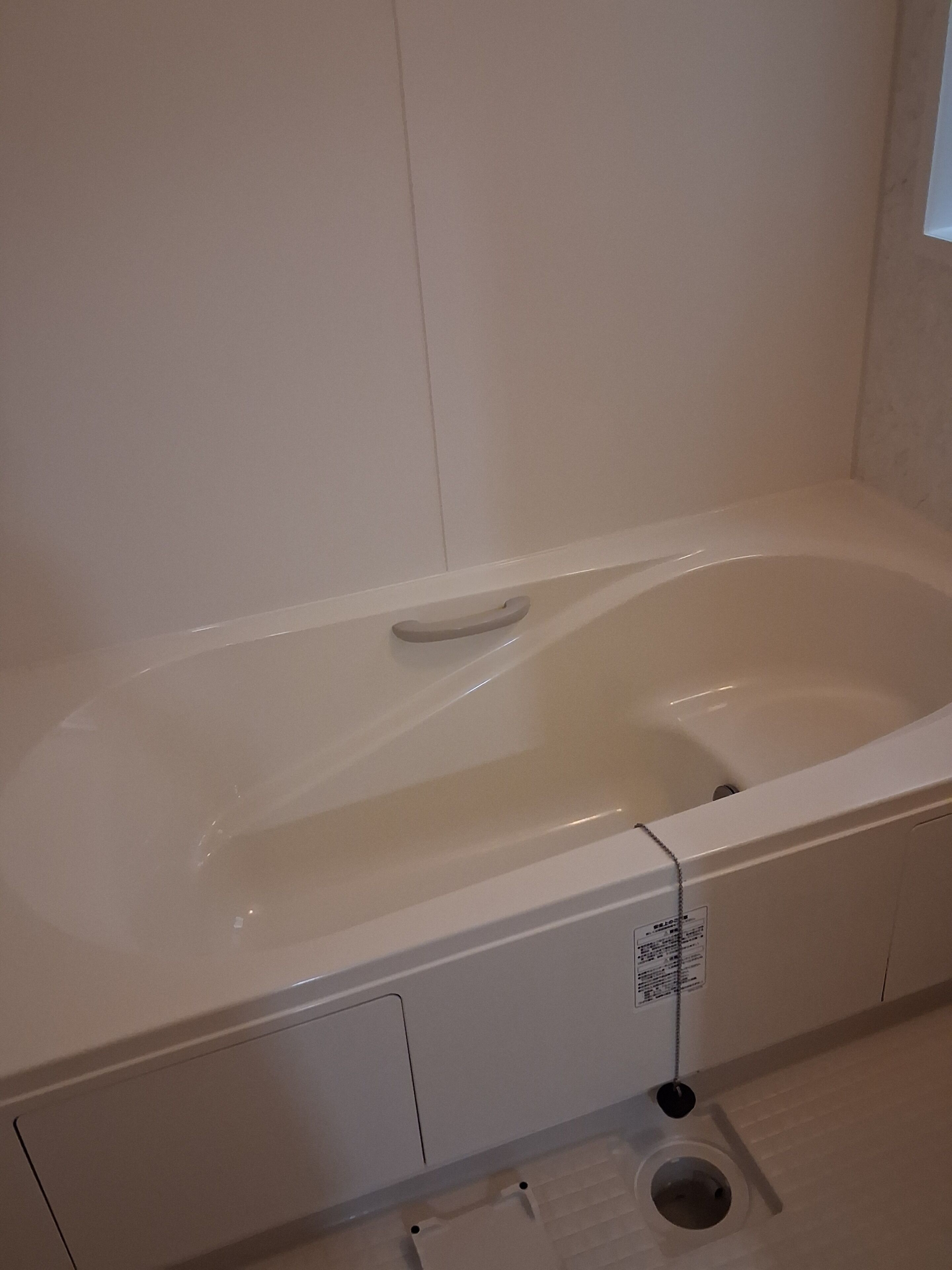 A white bathtub with a drain, a small shelf, and a control panel.