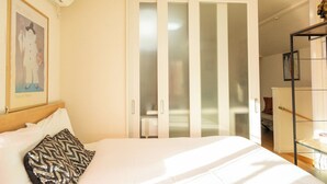 Et hotelværelse med en seng, en garderobe med glasdøre, et billede hængende på væggen og et lille bord med en lampe.