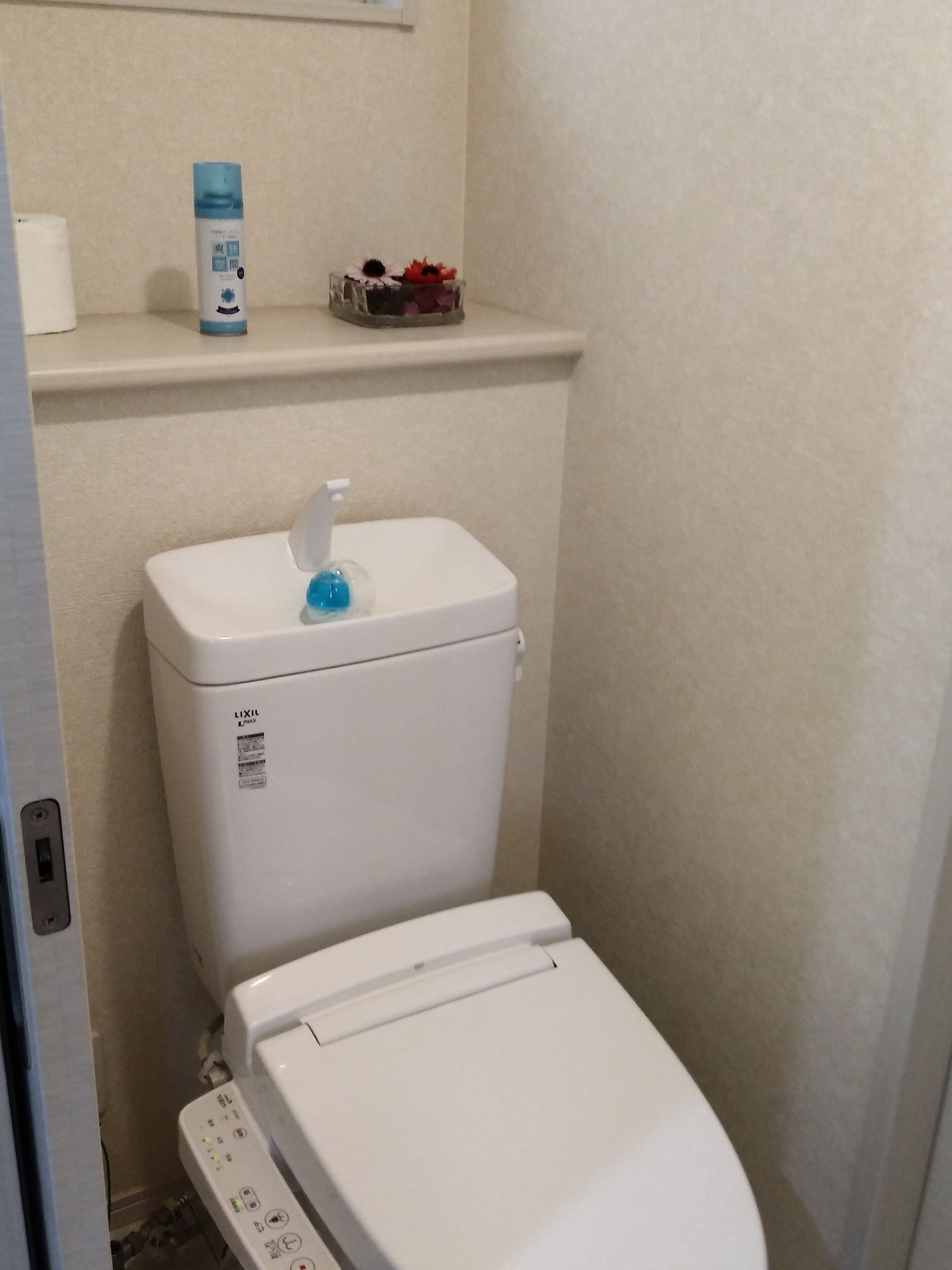A toilet with a control panel, a shelf with toiletries, and a small decorative item.