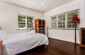 Comfortable room with a neatly made bed, wardrobe, and radiator, featuring two windows with blinds.