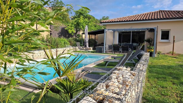 Un jardin avec une piscine, un patio couvert et un mur en pierre.