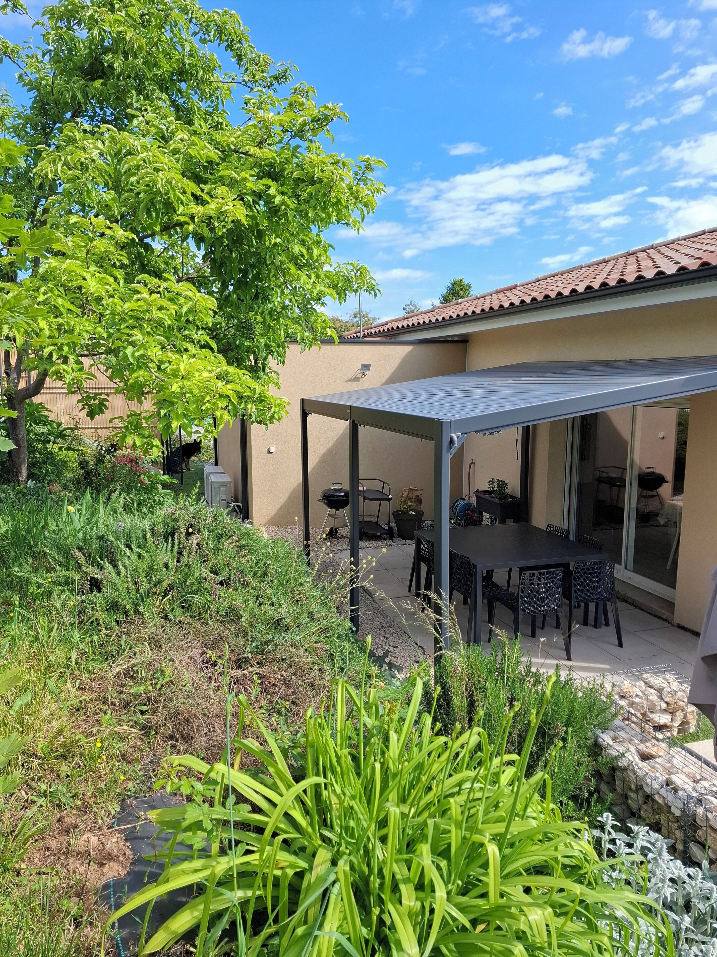 A patio area with a covered seating area, a barbecue grill, and a dining table with chairs.