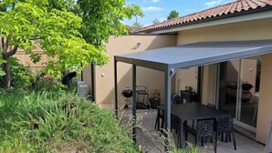 Un espace patio comprenant un coin salon couvert, un barbecue et une table à manger avec des chaises.