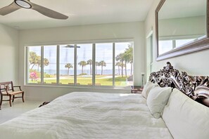Relax in this serene bedroom with a large bed and a view of the lush lawn and palm trees through the large window.