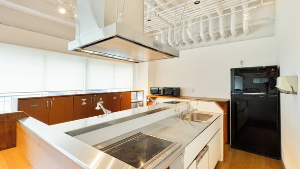A modern kitchen with stainless steel appliances, wooden cabinets, and a large island with a built-in stovetop. - Hostel Ogk (Osaka)
