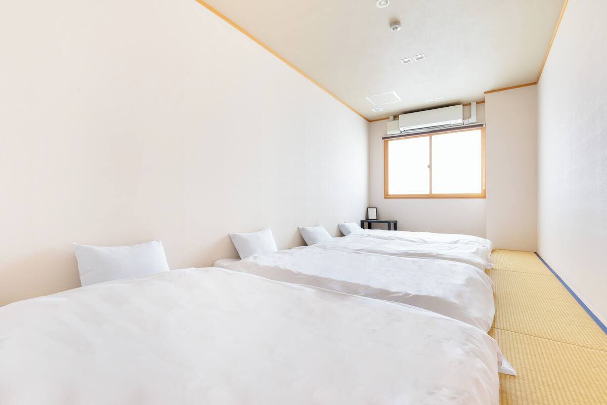 A hotel room with two beds, a window, and a ceiling air conditioner.