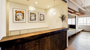 A reception desk with framed artwork, a wooden counter, and a modern interior with exposed ceilings and a large window. - Hostel Ogk (Osaka)
