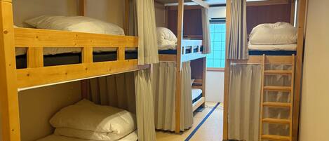 A dormitory-style room with bunk beds, a ladder, and a window with curtains.