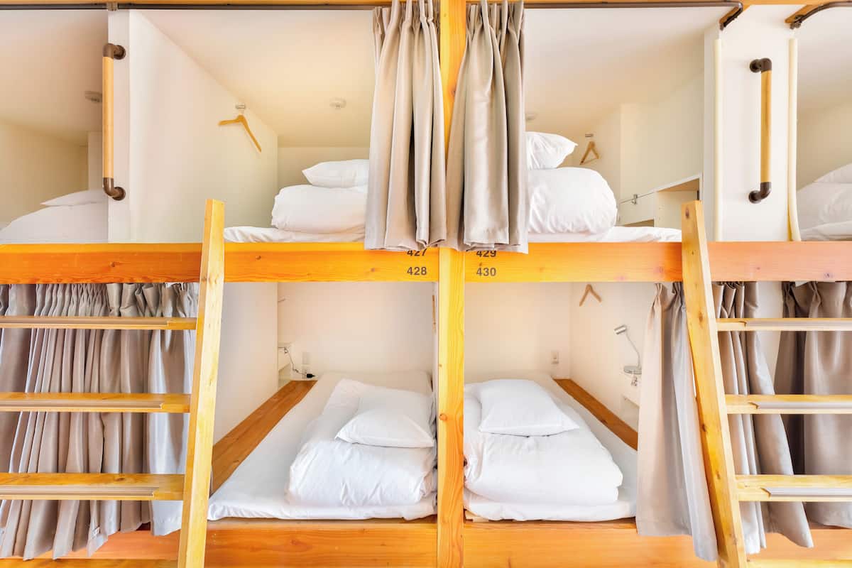 A bunk bed room with wooden frames, white bedding, and curtains.