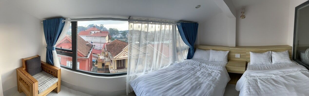 Habitación de hotel con un ventanal grande, dos camas, una silla de madera y vistas a edificios.