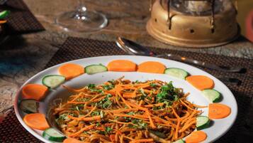 A plate of shredded carrots and cucumbers on a table with a candle and a glass of red drink.