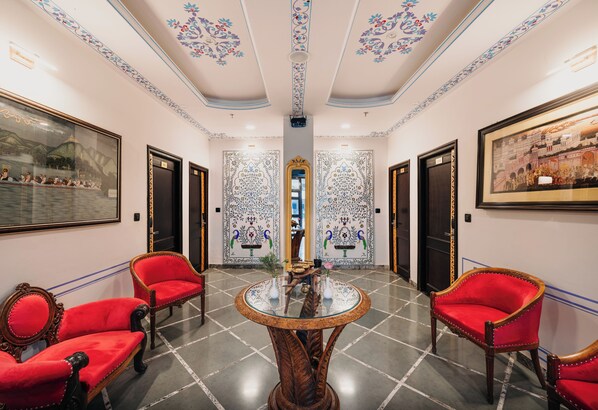 Un pasillo con una mesa redonda, sillas rojas y decoraciones de pared elaboradas.