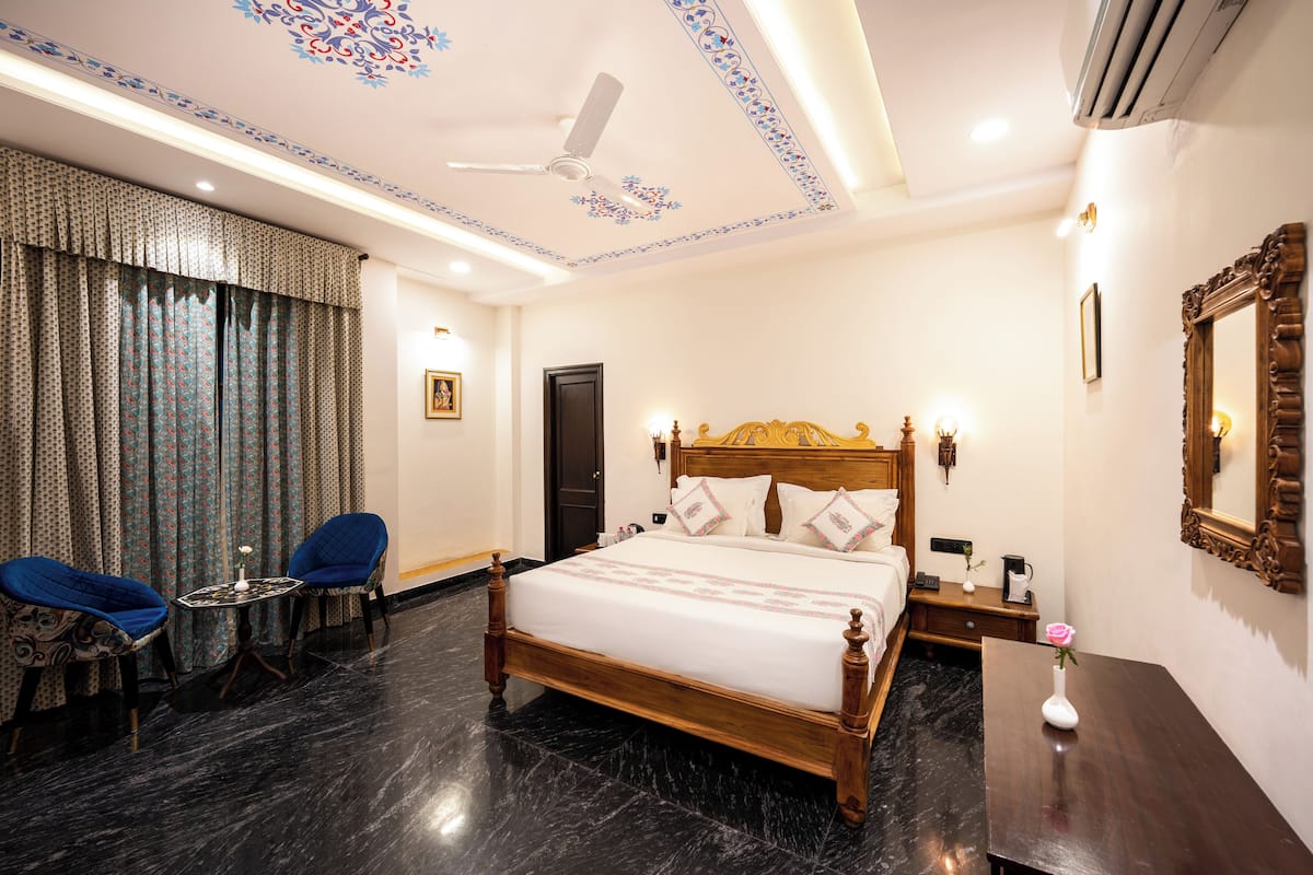 Ein Hotelzimmer mit einem großen Bett, zwei Stühlen, einem kleinen Tisch, einem Nachttisch und einem Spiegel.