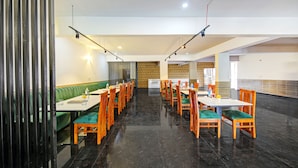 A spacious dining area with high tables and chairs, a green booth seating area, and a patterned wall in the background.