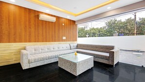 A modern lobby with a wooden wall, a grey sofa, a glass coffee table, and a view of greenery outside.
