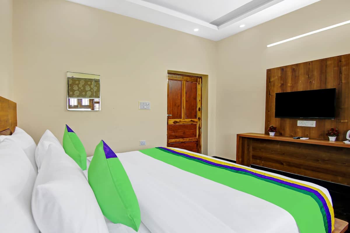 A hotel room with a bed, a TV, a wooden desk, and a door.