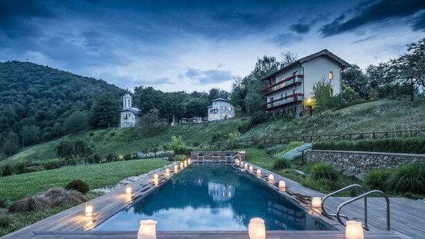 Una piscina con cubierta de madera y velas, rodeada de vegetación y una colina con edificios.