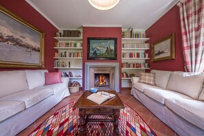 Un salón acogedor con chimenea, dos sofás blancos, una mesa de centro y estanterías llenas de libros.