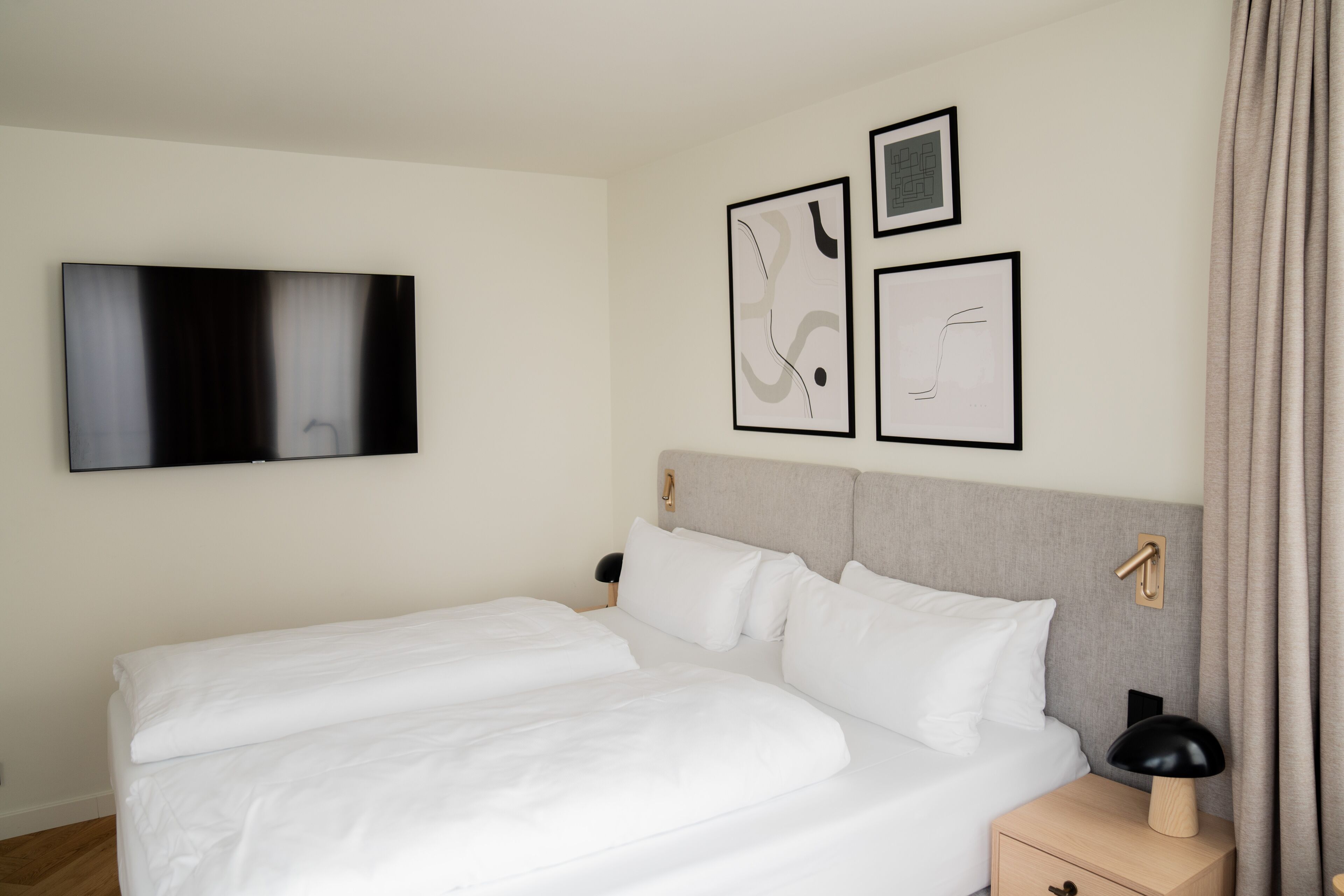 Una habitación de hotel moderna con una cama grande, un televisor de pantalla plana y tres obras de arte enmarcadas en la pared.