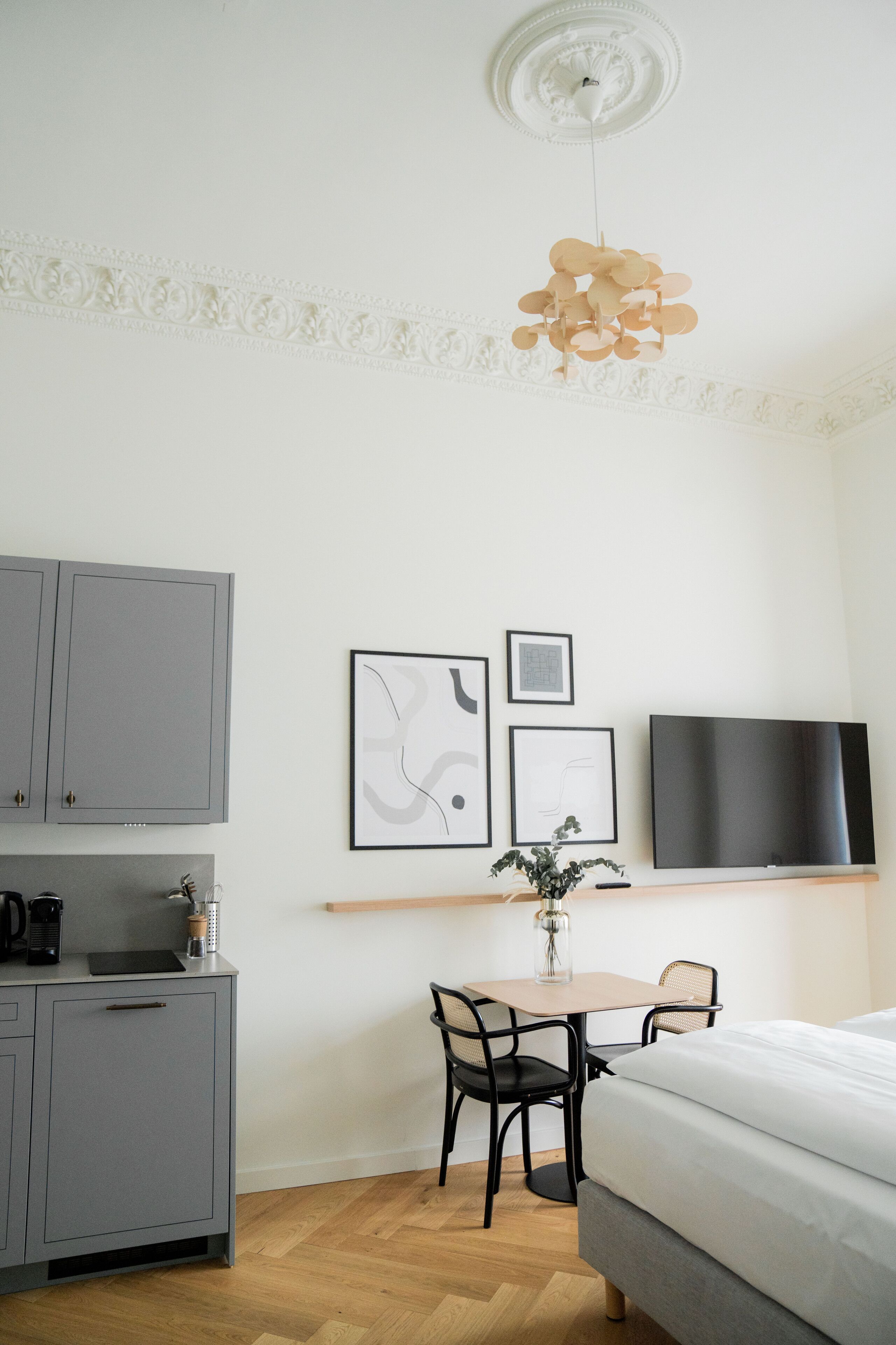 A modern hotel room with a bed, a desk with a chair, a television, and a kitchenette.