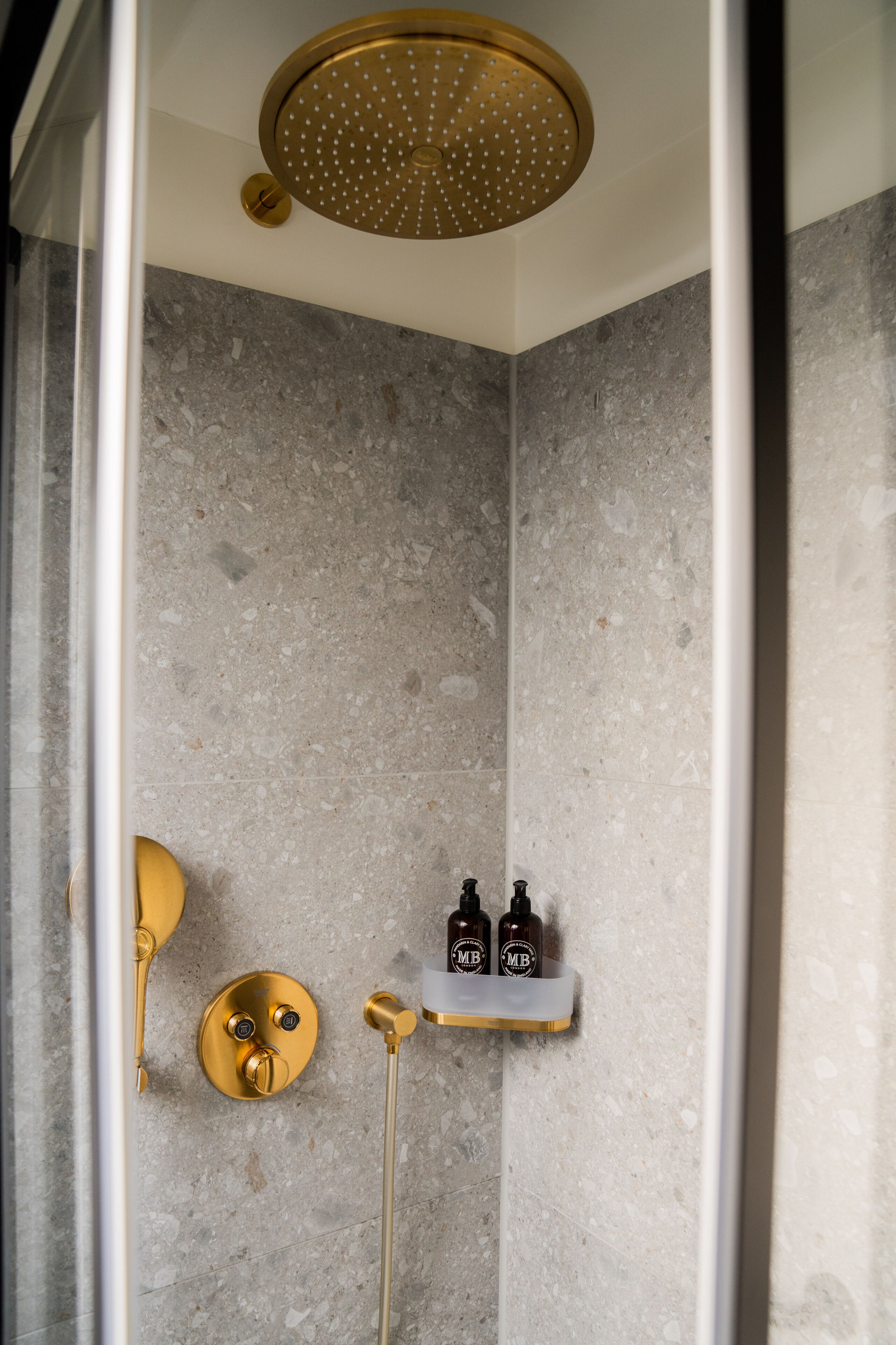Eine Dusche mit goldfarbenem Duschkopf, einem Wasserhahn aus Gold und einem Regal mit zwei Flaschen.