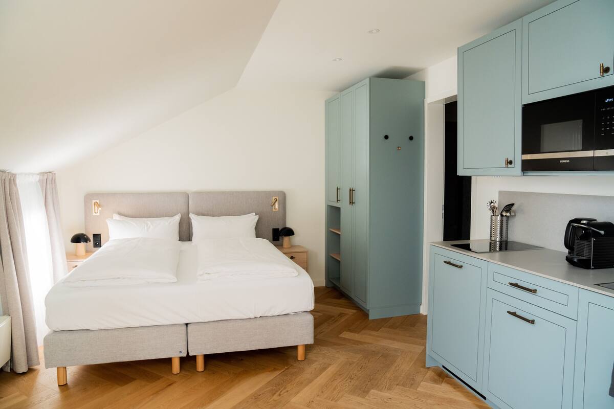 A bedroom with a bed, a nightstand, a wardrobe, and a kitchenette.
