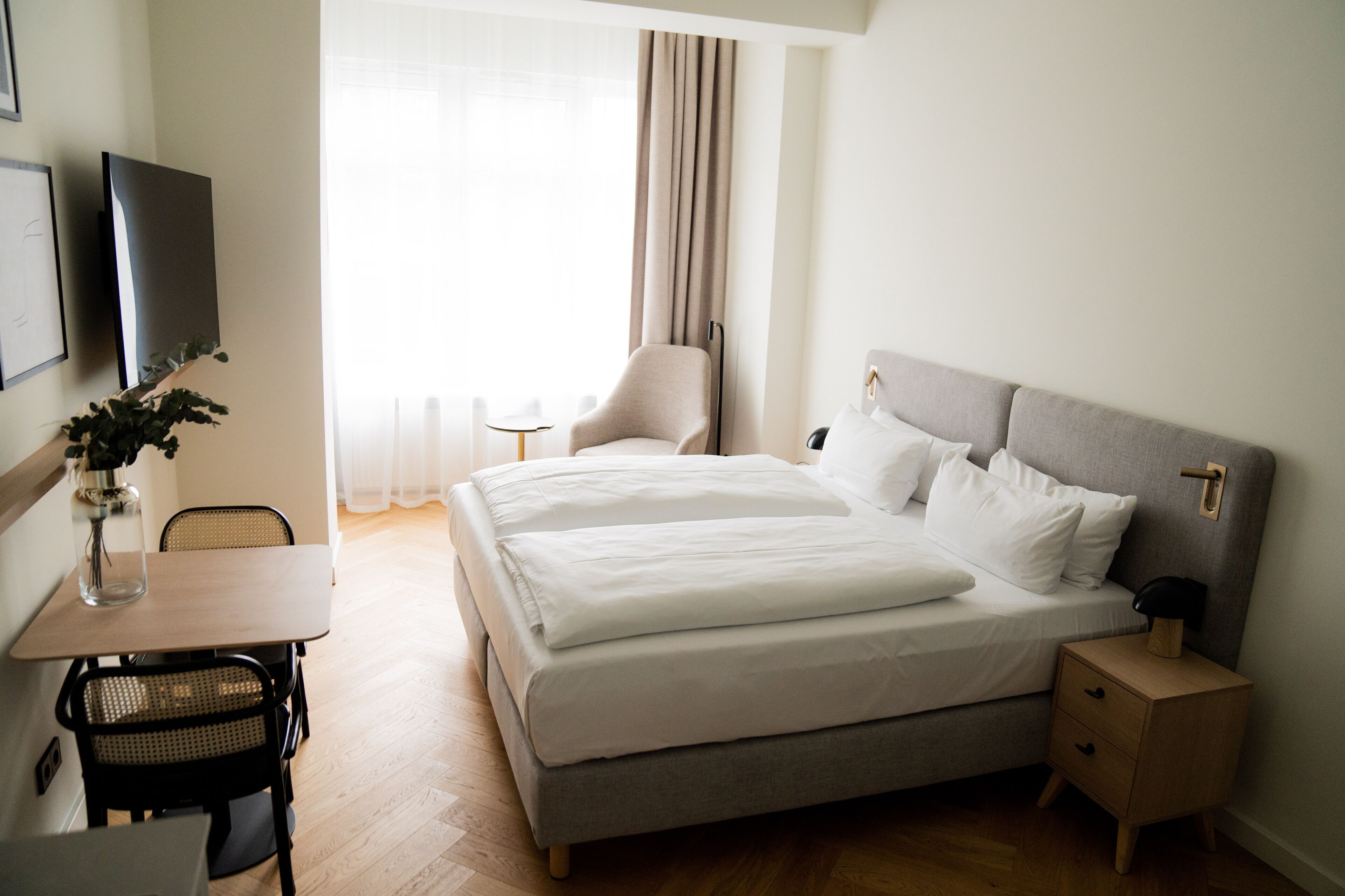 A hotel room with a bed, bedside table, chair, desk, and a TV.