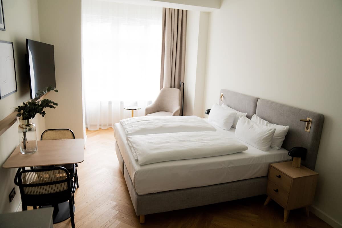 A hotel room with a bed, bedside table, chair, desk, and a TV.