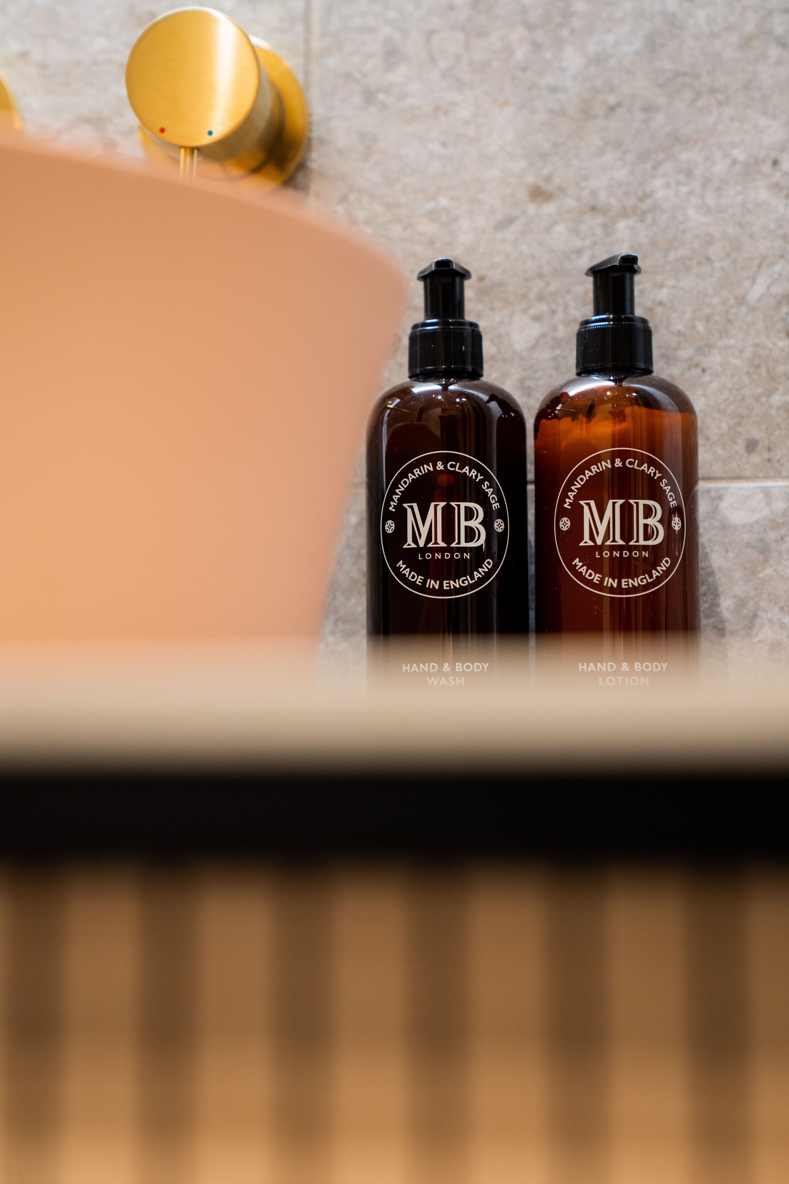 Two bottles of hand wash and body lotion with a gold faucet in the background.