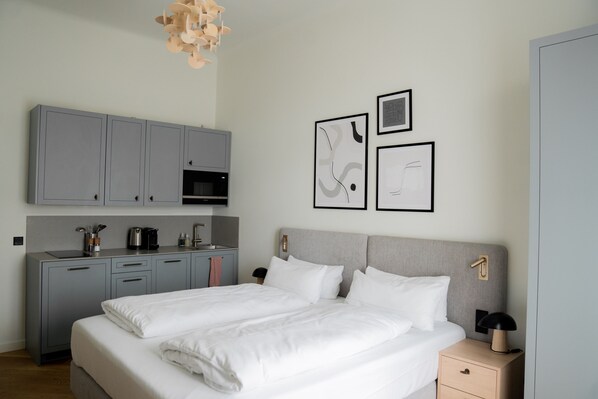Quarto de hotel moderno com uma cama grande, escrivaninha embutida e cozinha compacta.