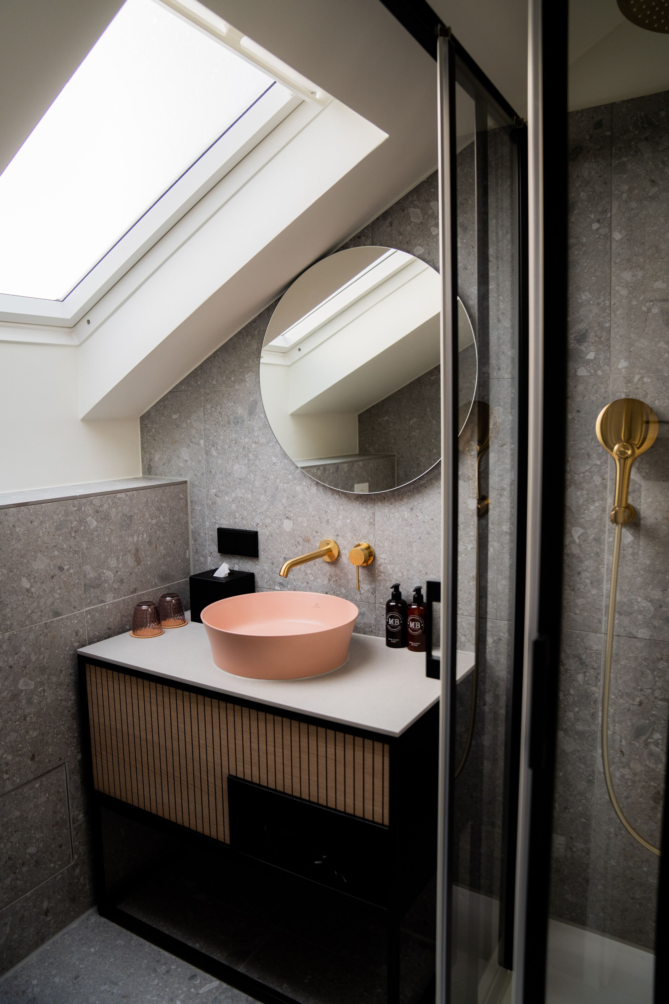 Een moderne badkamer met dakraam, een rond roze wastafel en een douchecabine.