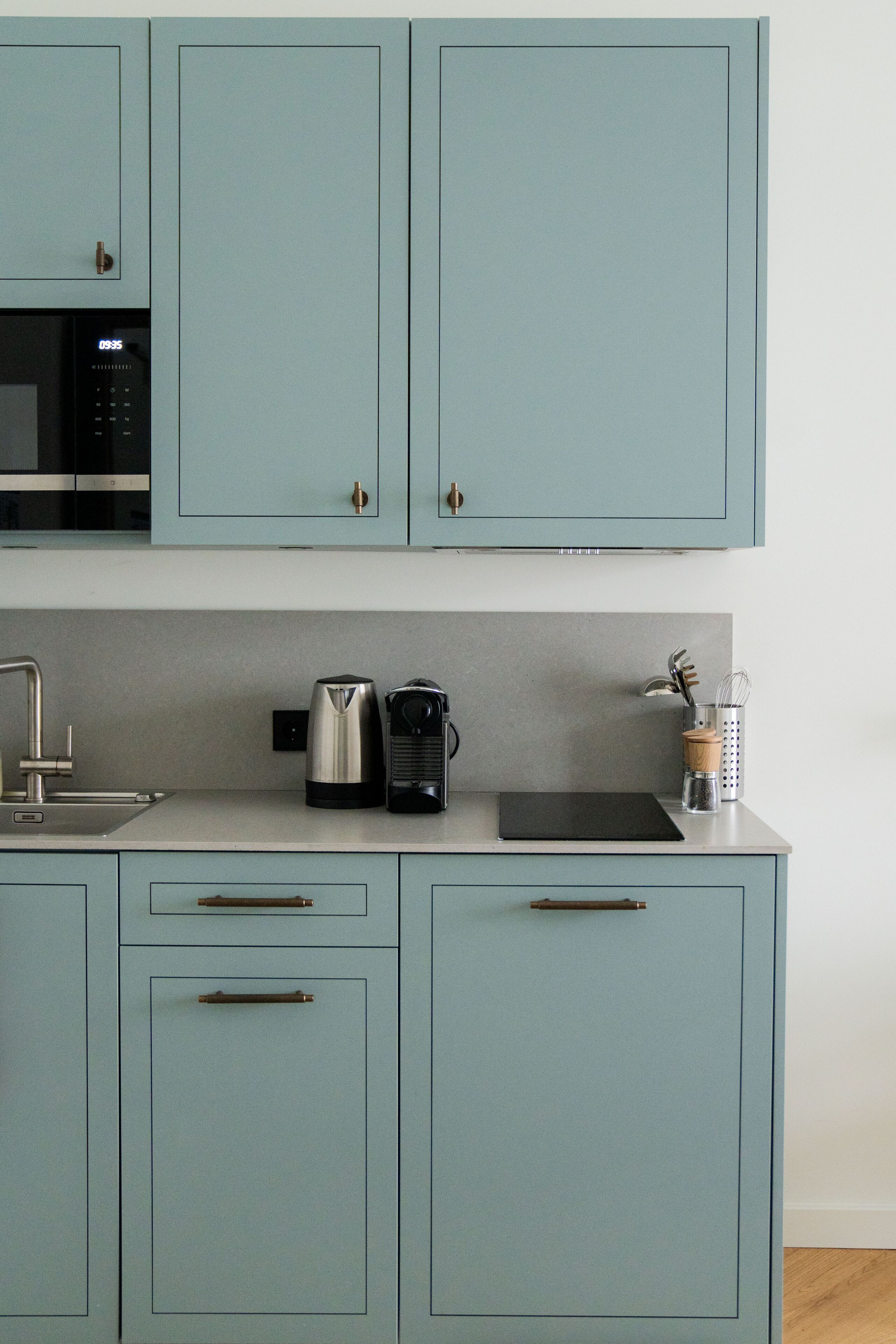 Una cucina con mobili azzurri, un lavandino in acciaio inossidabile, un bollitore, una macchina da caffè e una spezieria.
