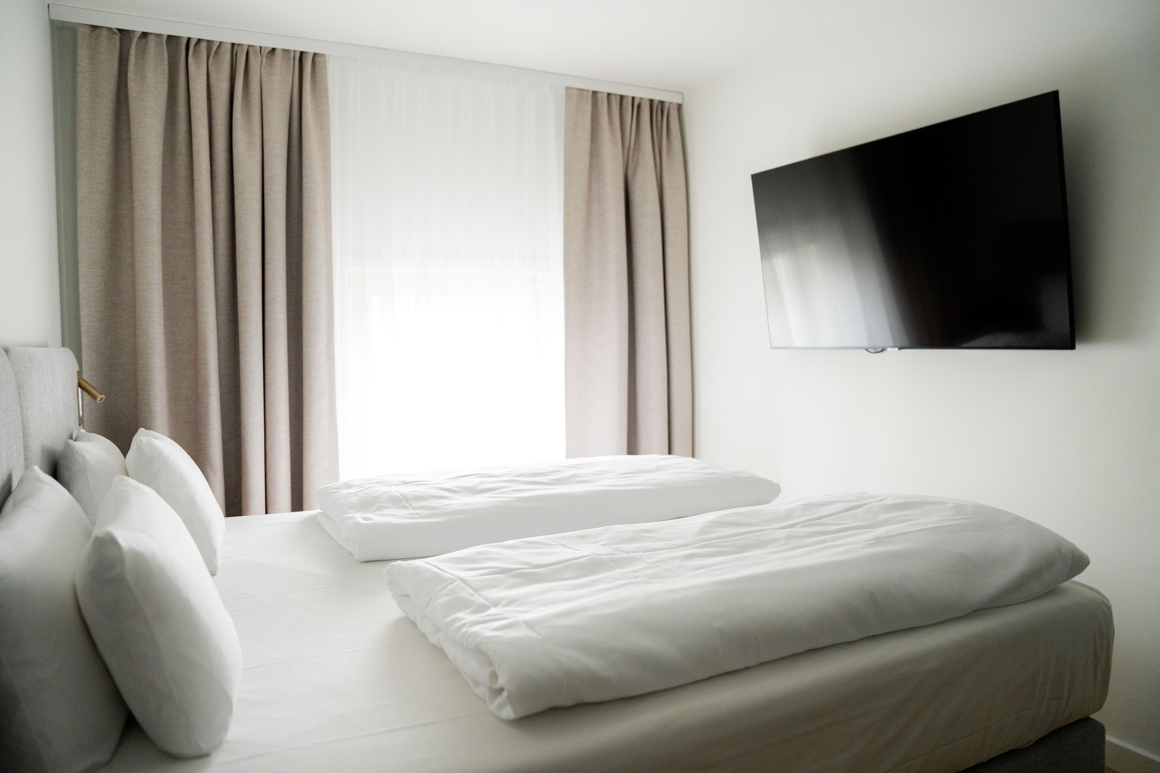 Une chambre d’hôtel équipée d’un lit, d’oreillers, d’un téléviseur à écran plat fixé au mur et de rideaux.