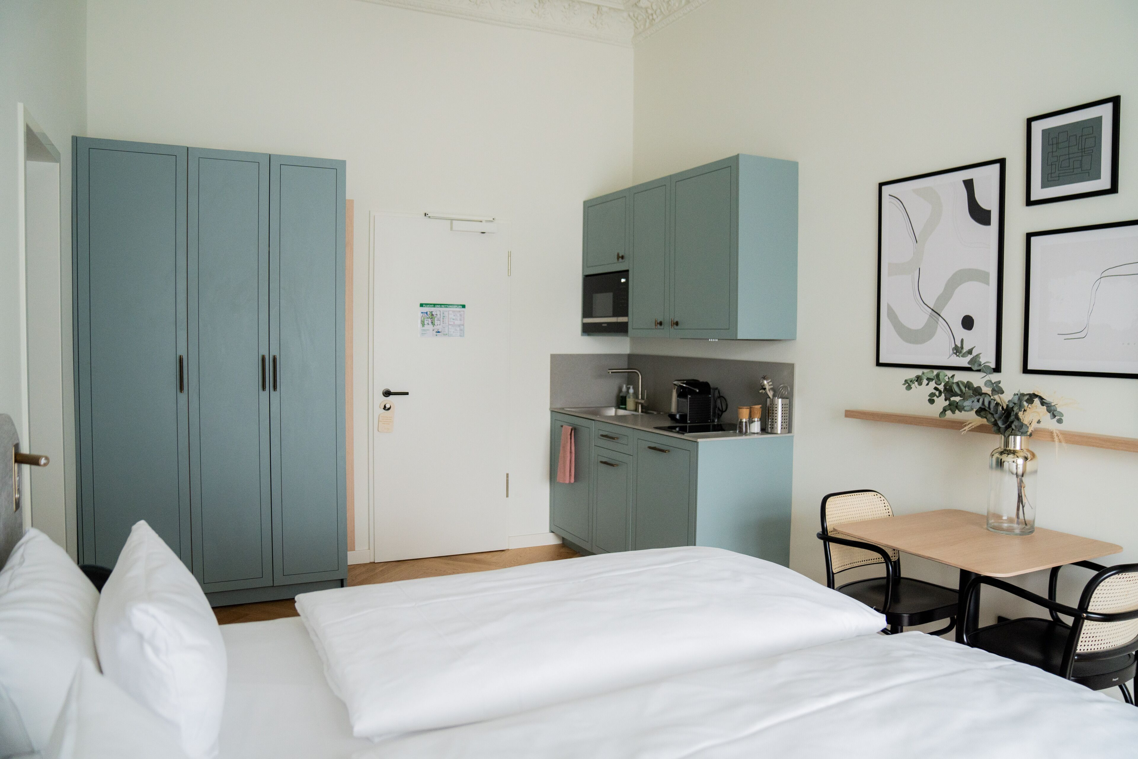Une chambre comprenant un lit, un bureau avec une chaise, un coin cuisine et une armoire.