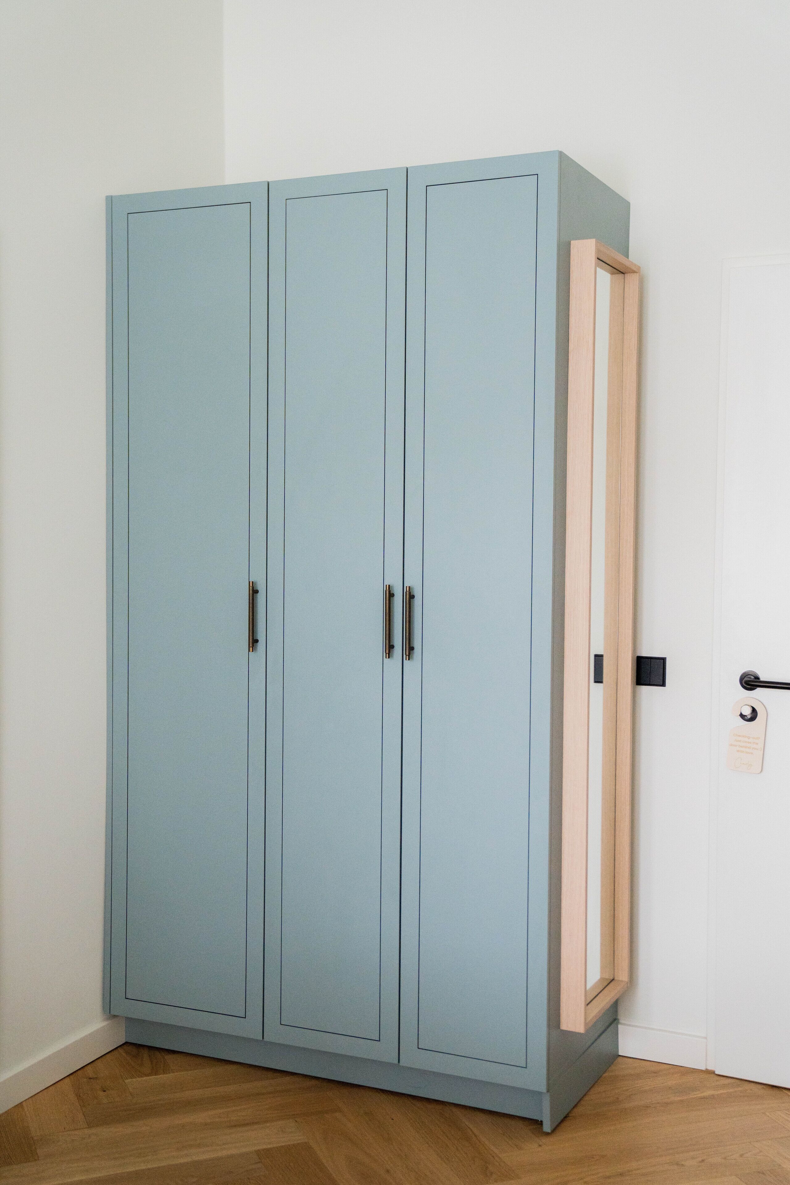 Een lichtblauwe kast met twee deuren en een houten frame aan de rechterkant.