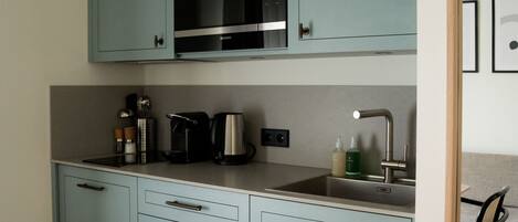 A kitchen with light blue cabinets, a microwave, a coffee maker, and a sink.