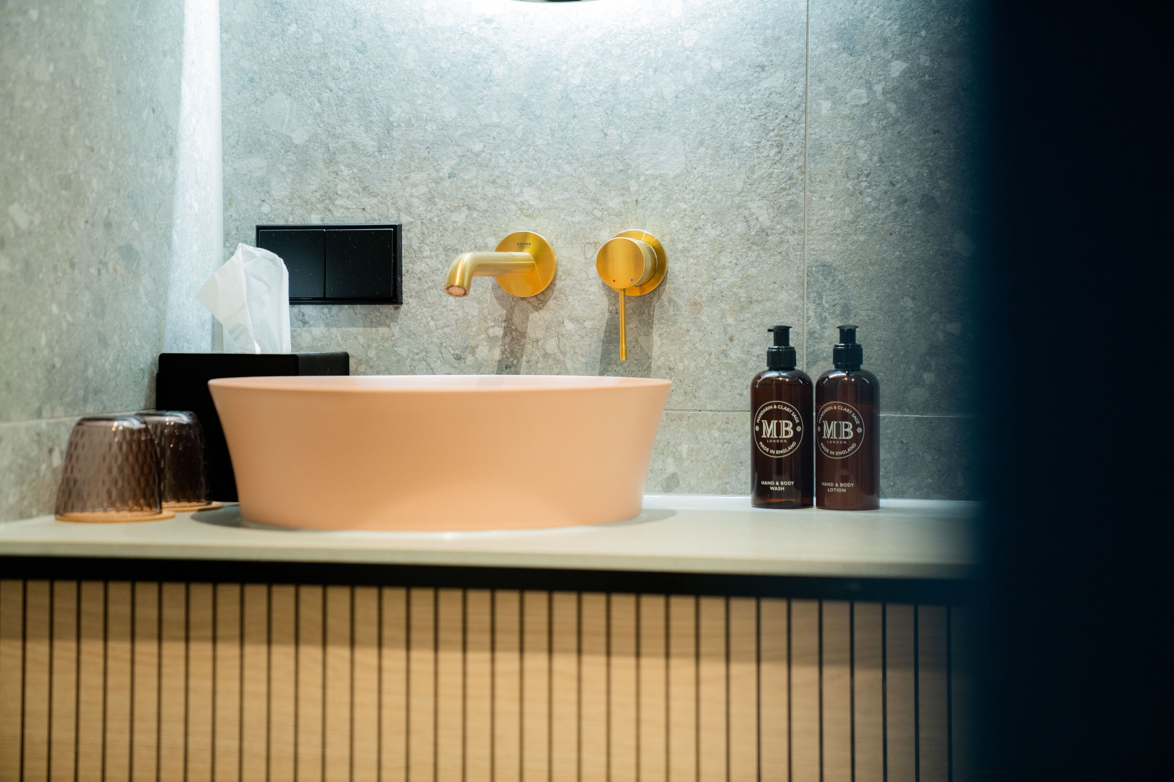 A bathroom with a large pink sink, a gold faucet, and two bottles of hand and body lotion on the counter.