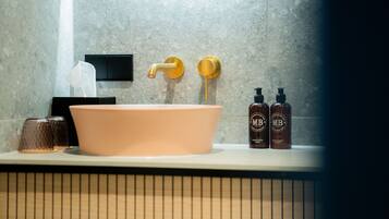 A bathroom with a large pink sink, a gold faucet, and two bottles of hand and body lotion on the counter.