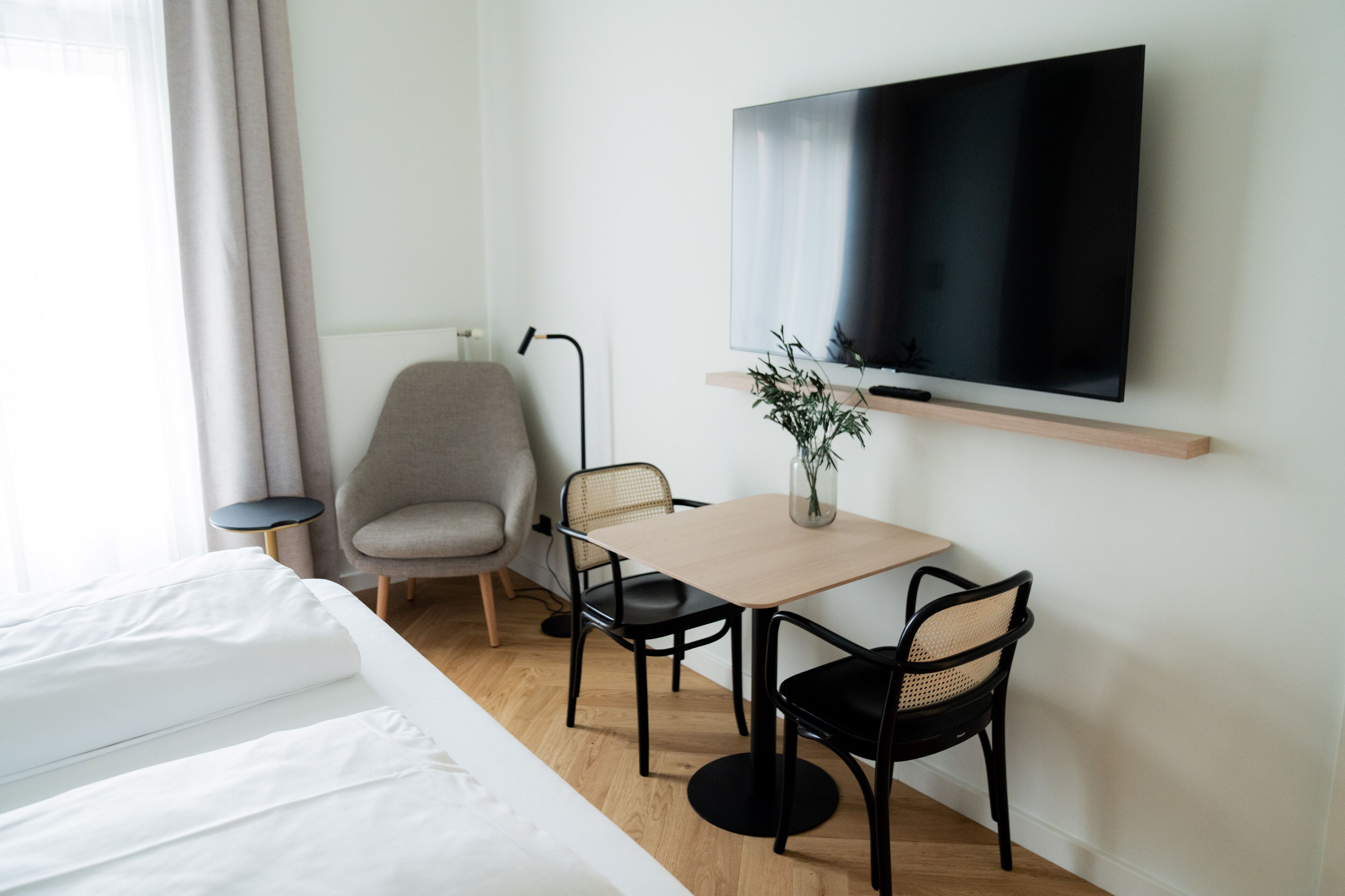 A hotel room with a bed, a desk with two chairs, a TV mounted on the wall, and a lamp.