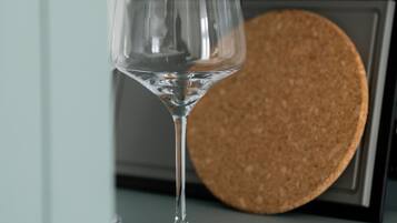 A clear glass wine glass on a shelf with a cork coaster and white ceramic mugs in the background.