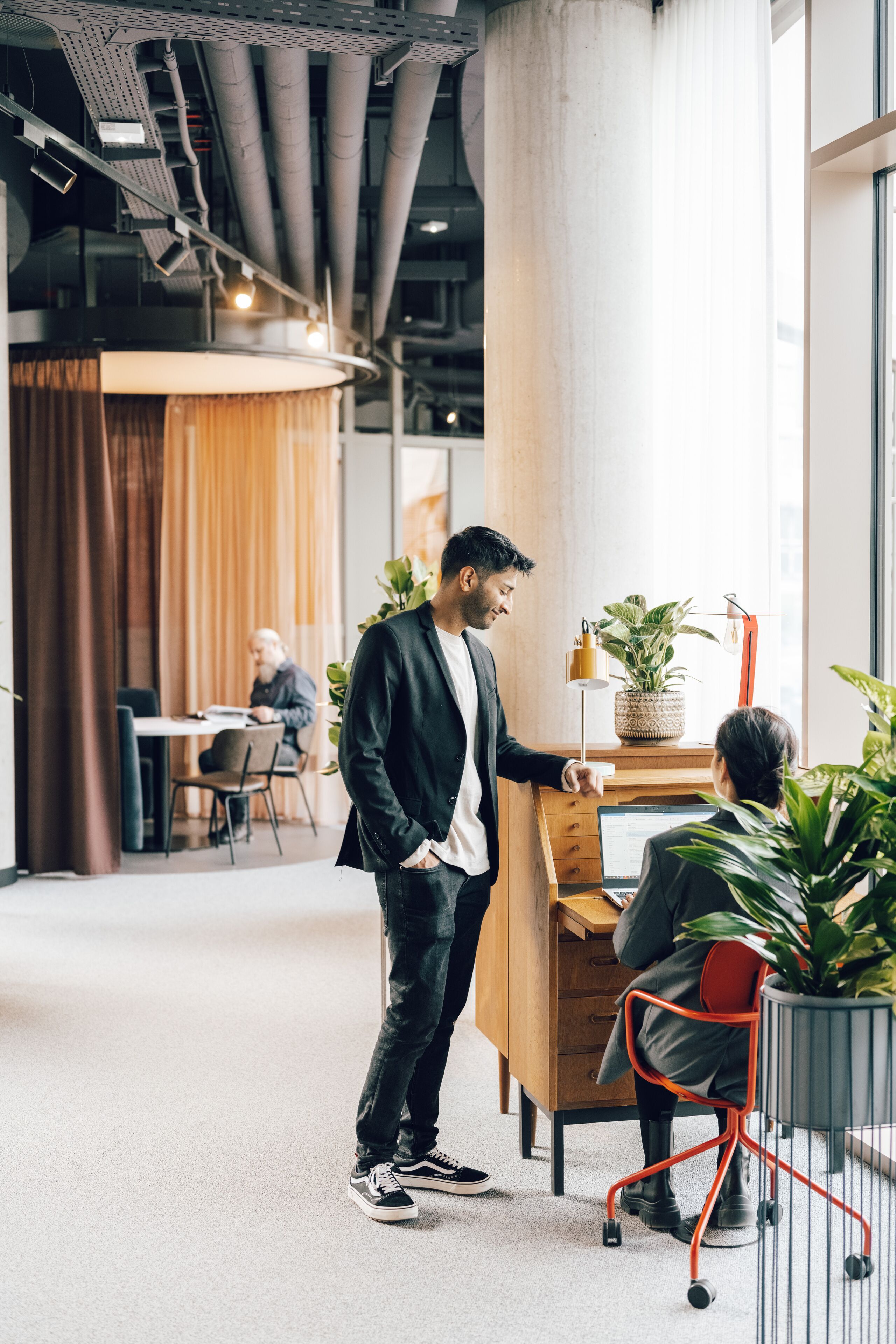 A modern office space with a large column, a desk with a computer, and a plant.