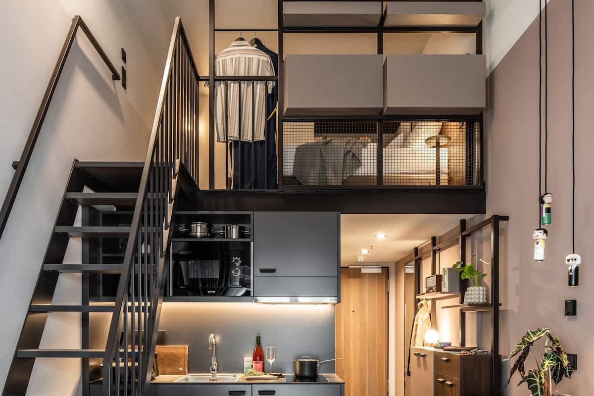 Una cocina moderna con una isla central, un comedor con un tablero de ajedrez y una escalera que sube a un nivel superior.