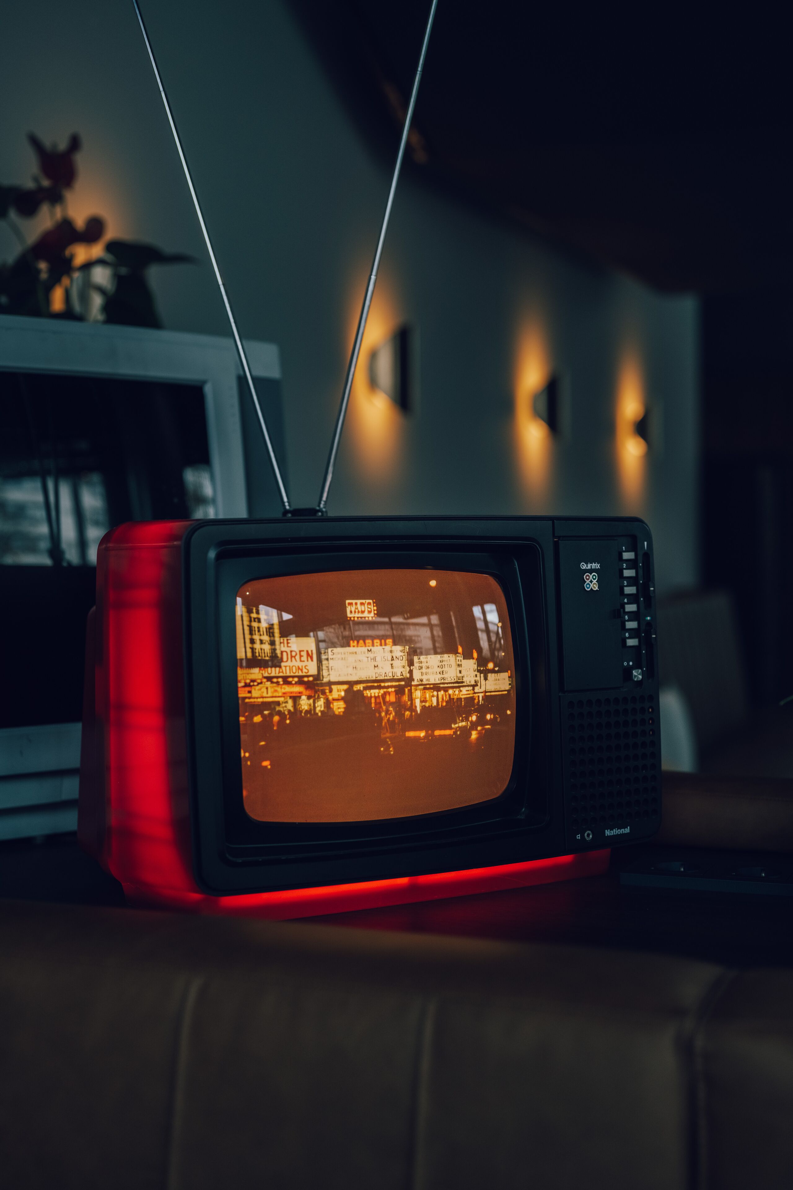 Un televisor antiguo sobre un soporte rojo, mostrando un paisaje urbano.